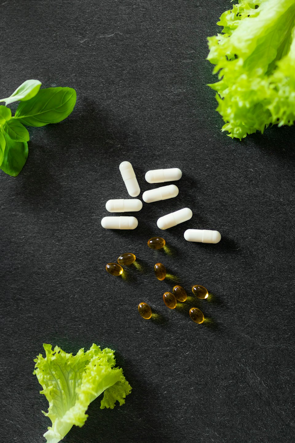 Tabletten und frische Kräuter auf dunklem Untergrund.